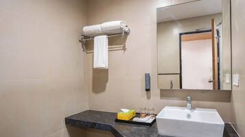 Un baño con encimera de mármol, un lavabo blanco, un perchero con una toalla enrollada, un espejo y un pequeño estuche de artículos de tocador.