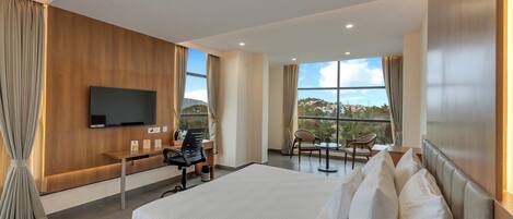 Habitación de hotel moderna con una cama grande, un escritorio con silla, televisión y balcón con vistas.