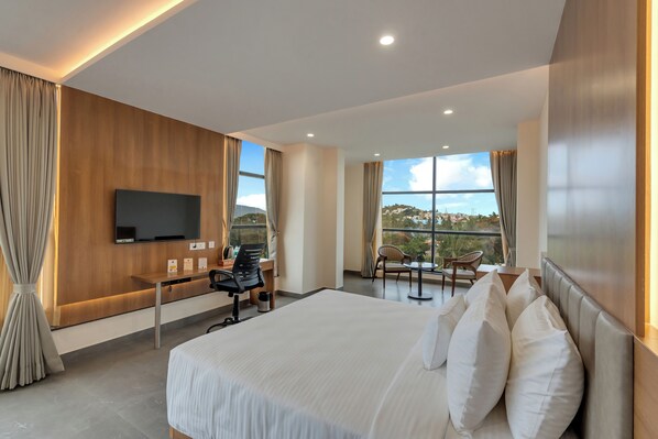 Habitación de hotel moderna con una cama grande, un escritorio con silla, televisión y balcón con vistas.