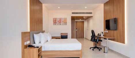 A modern hotel room with a bed, bedside table, desk, chair, and a TV mounted on the wall.