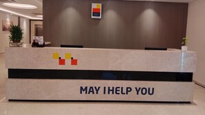 A hotel reception desk with a 'May I Help You' sign, a MySpace Hotels Kenilworth sign, and a vertical wooden panel.