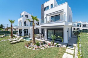 Ein modernes, zweistöckiges Haus mit Pool, Sitzgelegenheit im Freien und einem gepflegten Garten.