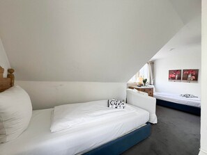 A bedroom with a single bed, a nightstand, a dresser, and a window with curtains.