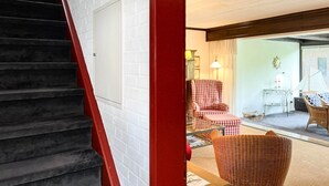 A staircase with a red handrail leading to a room with checkered chairs and a wicker chair. - Vacation apartment Kerstin - The vacation home Kerstin offers you with approx110m² a lot of space. (Sylt)