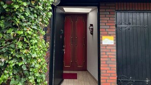 A building entrance with a red door, a black gate, and a brick wall partially covered by ivy. - Vacation apartment Kerstin - The vacation home Kerstin offers you with approx110m² a lot of space. (Sylt)
