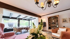 A cozy living room with a checkered sofa, a glass coffee table with a floral arrangement, a wicker armchair, and a television on a wooden stand. - Vacation apartment Kerstin - The vacation home Kerstin offers you with approx110m² a lot of space. (Sylt)