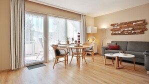 A modern living room with a grey sofa, a dining table with wicker chairs, a floor lamp, and a wall art of fish.