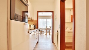 A narrow hallway with a kitchen area on the left, a dining area with a table and chairs in the center, and a bathroom with a toilet and sink on the right.