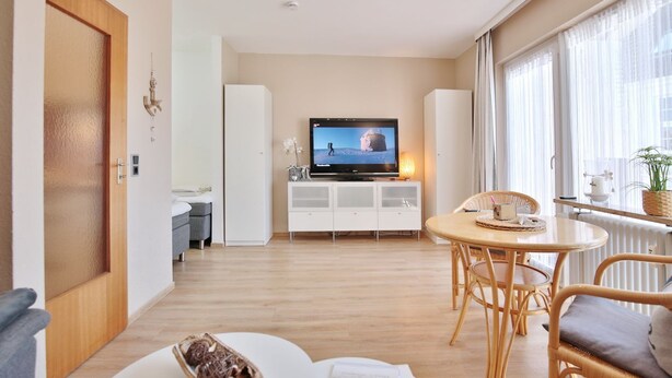 A modern living room with a television, dining area, and a large window with curtains.