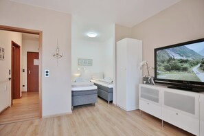 A modern hotel room with a bed, a seating area, a television, and a view of a mountainous landscape.