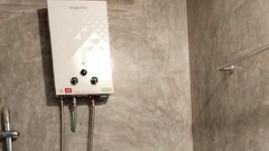 Un baño con inodoro, ducha y calentador de pared.