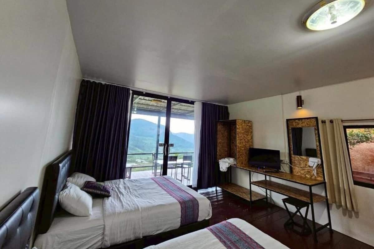 A hotel room with two beds, a desk with a TV, a window with curtains, and a view of the mountains.