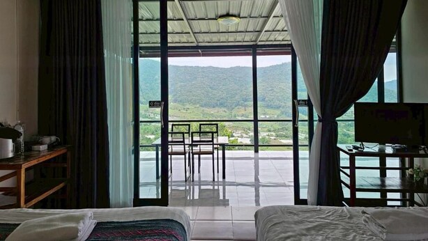 Habitación de hotel con cama, escritorio y vista a un paisaje montañoso a través de amplias ventanas.