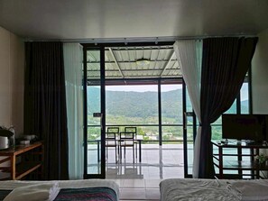 A hotel room with a bed, a desk, and a view of a mountainous landscape through large windows. - Doymoktawanview (Chom Thong)