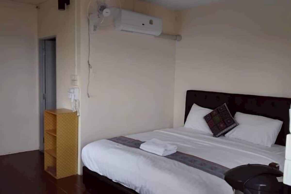 A hotel room with a bed, a bedside table, an air conditioning unit, and a wooden shelf.