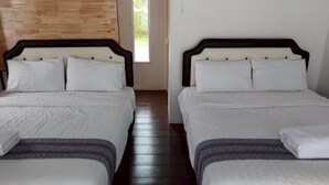 Dos camas con sábanas blancas y cabeceros de madera en una habitación con suelo de madera y una ventana.