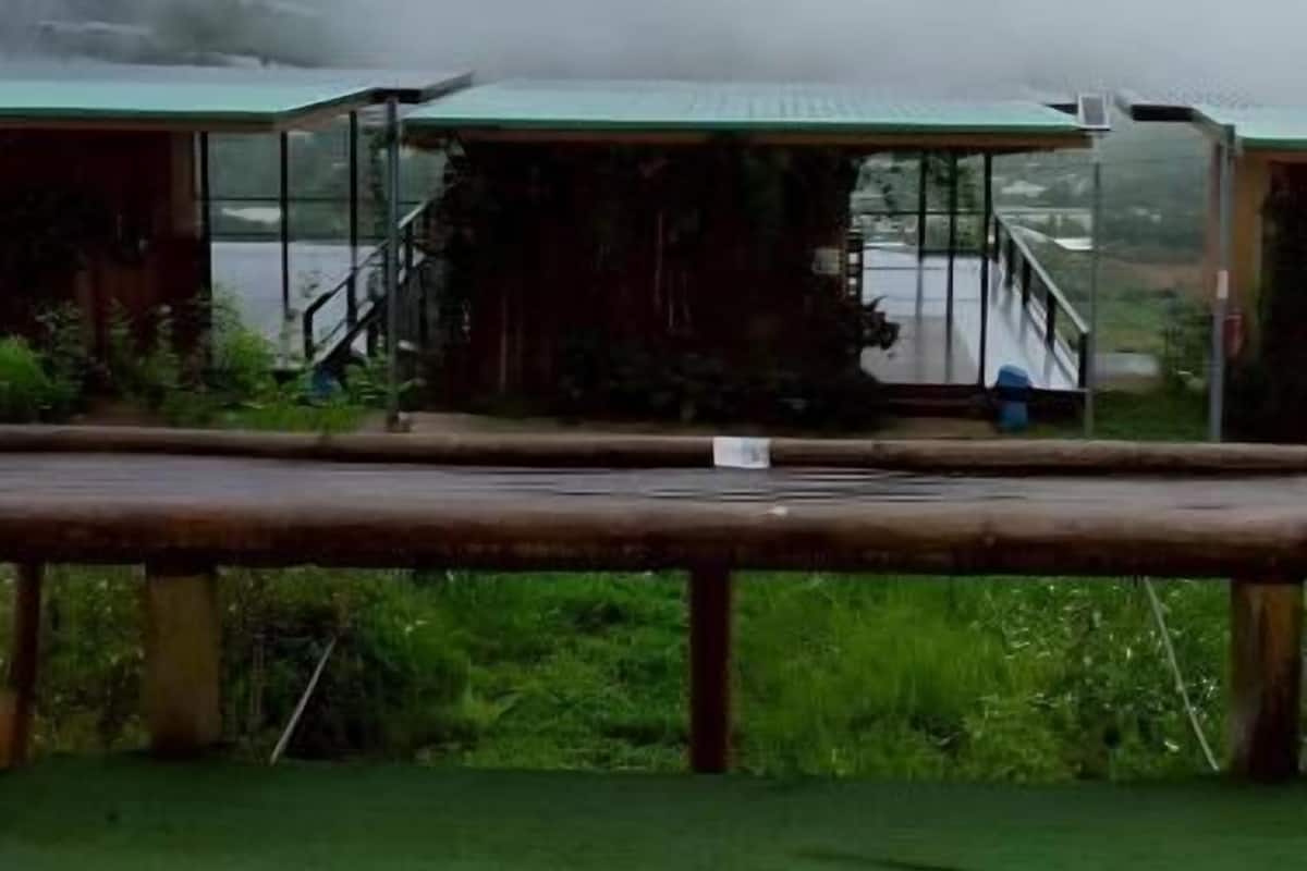 A rustic cabin with a green roof, a wooden deck, and a view of mist-covered mountains.
