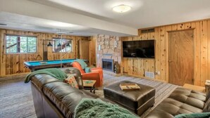 A cozy living room with a pool table, leather sofa, and a flat-screen TV mounted on the wall. - Serenity Pikes Peak Cabin with Hot Tub & Dog Friendly (Cascade-Chipita Park, CO)