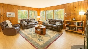 A cozy living room with wooden paneled walls, a brown leather sofa set, a coffee table, and a bookshelf. - Serenity Pikes Peak Cabin with Hot Tub & Dog Friendly (Cascade-Chipita Park, CO)