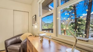 A room with a wooden desk, a brown leather chair, a small airplane model, and a window with a view of trees and mountains. - Serenity Pikes Peak Cabin with Hot Tub & Dog Friendly (Cascade-Chipita Park, CO)