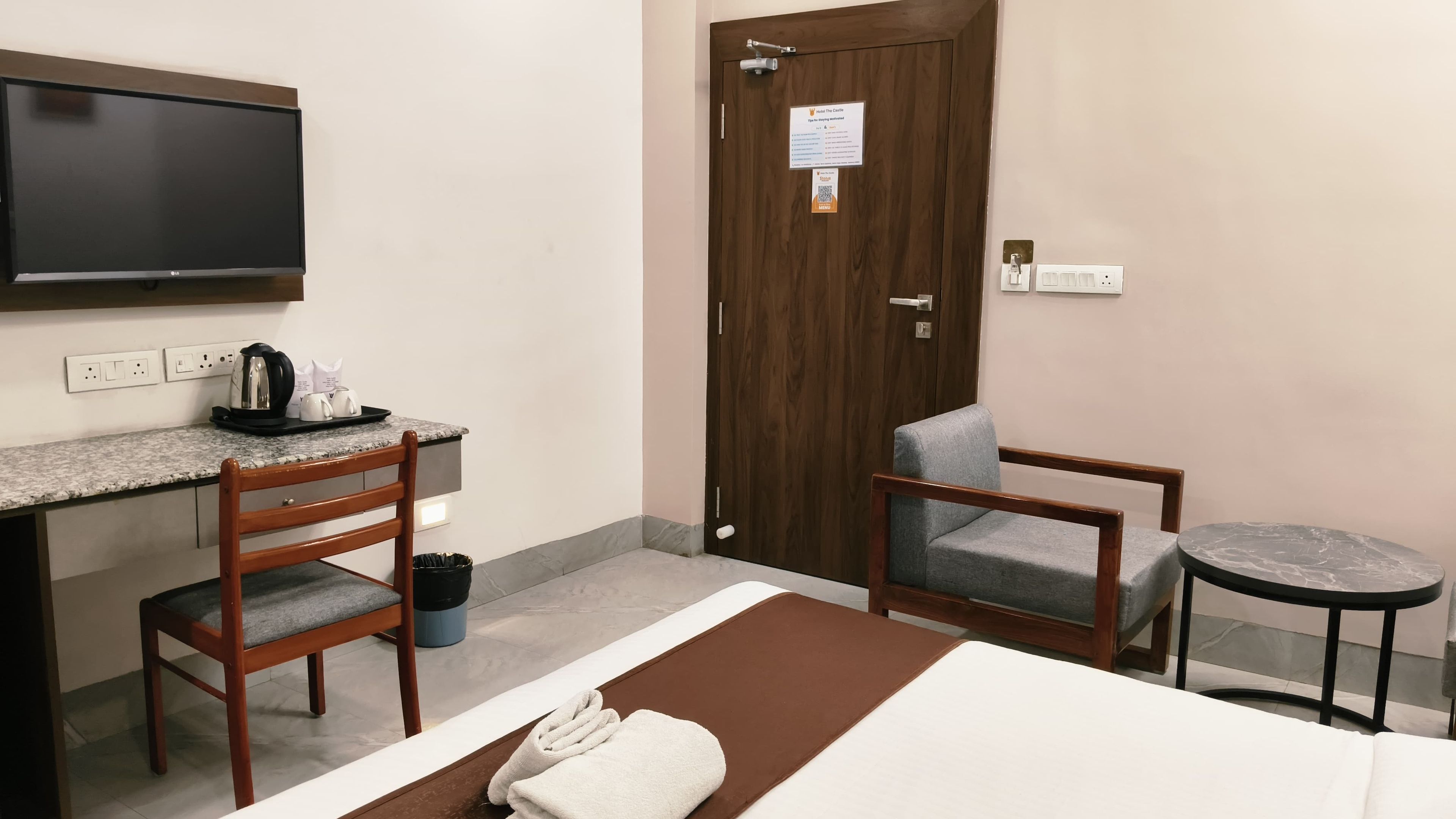 A hotel room with a bed, a desk, a chair, a TV, and a door.