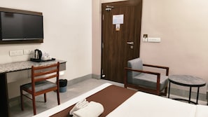 Una habitación de hotel con cama, escritorio, silla, televisor y puerta.