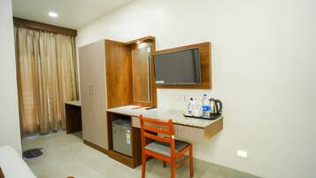 A compact hotel room with a kitchenette, a single bed, a desk with a chair, a television, and a small refrigerator.