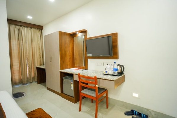 Habitación de hotel pequeña con kitchenette, una cama individual, un escritorio con silla, televisión y un refrigerador compacto.