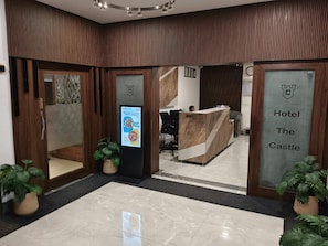 Zona de recepción de un hotel con mostrador de recepción, una pantalla digital mostrando información y un cartel con el nombre del hotel.