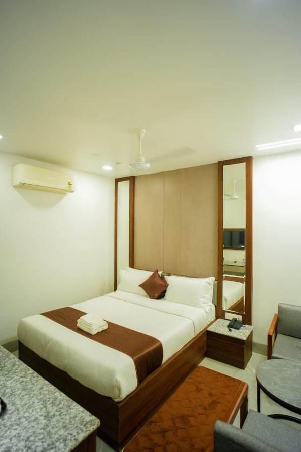 A hotel room with a bed, bedside table, chair, and a mirror.