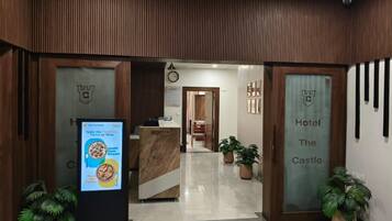 A hotel reception area with a reception desk, a clock, and potted plants.