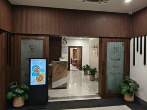 Zona de recepción de hotel con mostrador, un reloj y plantas en macetas.