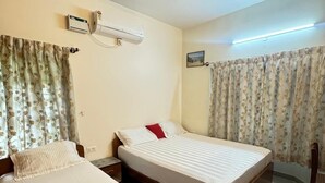 Una camera d'albergo con due letti singoli, una ventola a soffitto, un condizionatore d'aria e tende floreali.