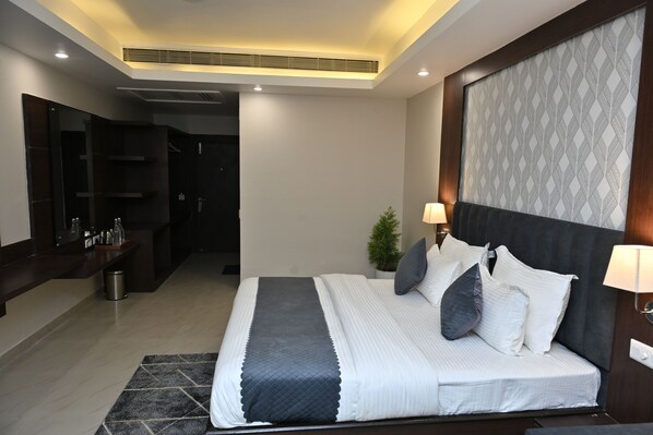 A modern bedroom with a large bed, bedside lamps, a small plant, and a dark headboard.