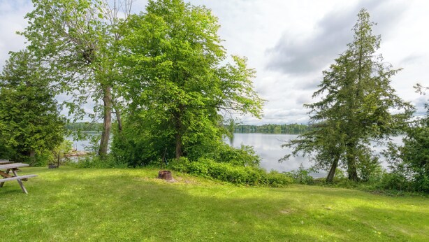 A grassy area with a picnic table and a bench, surrounded by trees and a lake. - Cozy Lake Escape: 2-Bed with Bunk, Sleeps 4, Full Kitchen & AC (Perth Road)