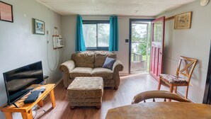 A living room with a sofa, ottoman, TV, and wooden table. - Cozy Lake Escape: 2-Bed with Bunk, Sleeps 4, Full Kitchen & AC (Perth Road)