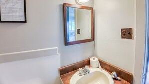 A bathroom with a sink, mirror, light fixture, and a framed informational sign. - Cozy Lake Escape: 2-Bed with Bunk, Sleeps 4, Full Kitchen & AC (Perth Road)