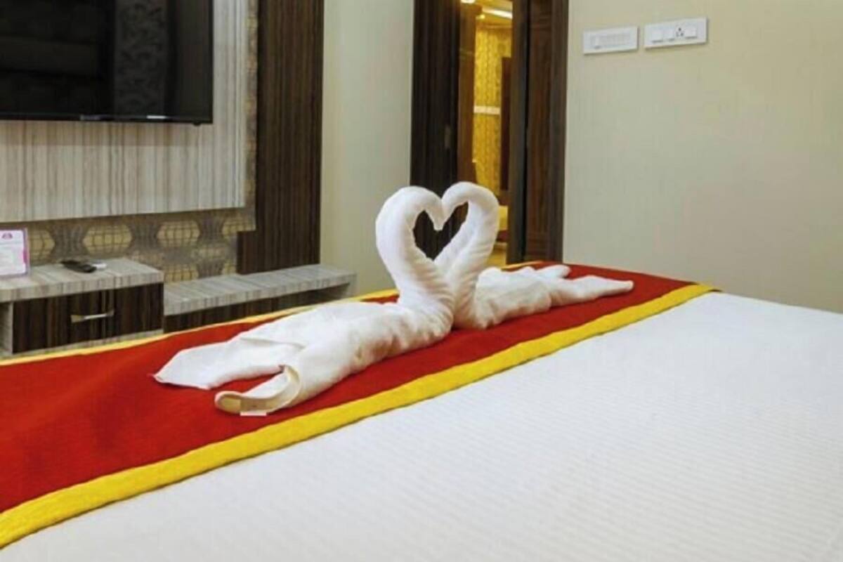 A hotel room with a bed, a heart-shaped towel, a red and yellow bedspread, a television, and a mirror.