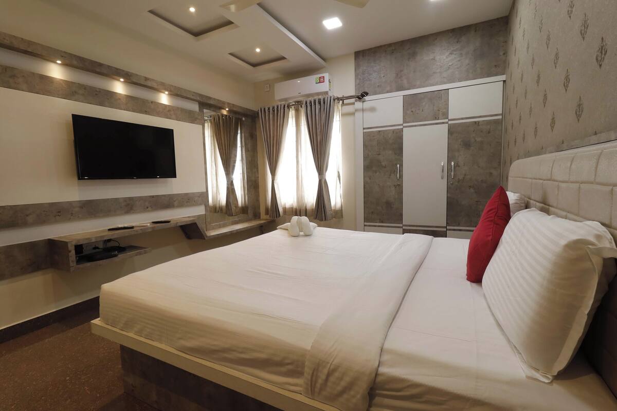 A hotel room with a large bed, a flat-screen TV mounted on the wall, a wardrobe, and a curtain-covered window.
