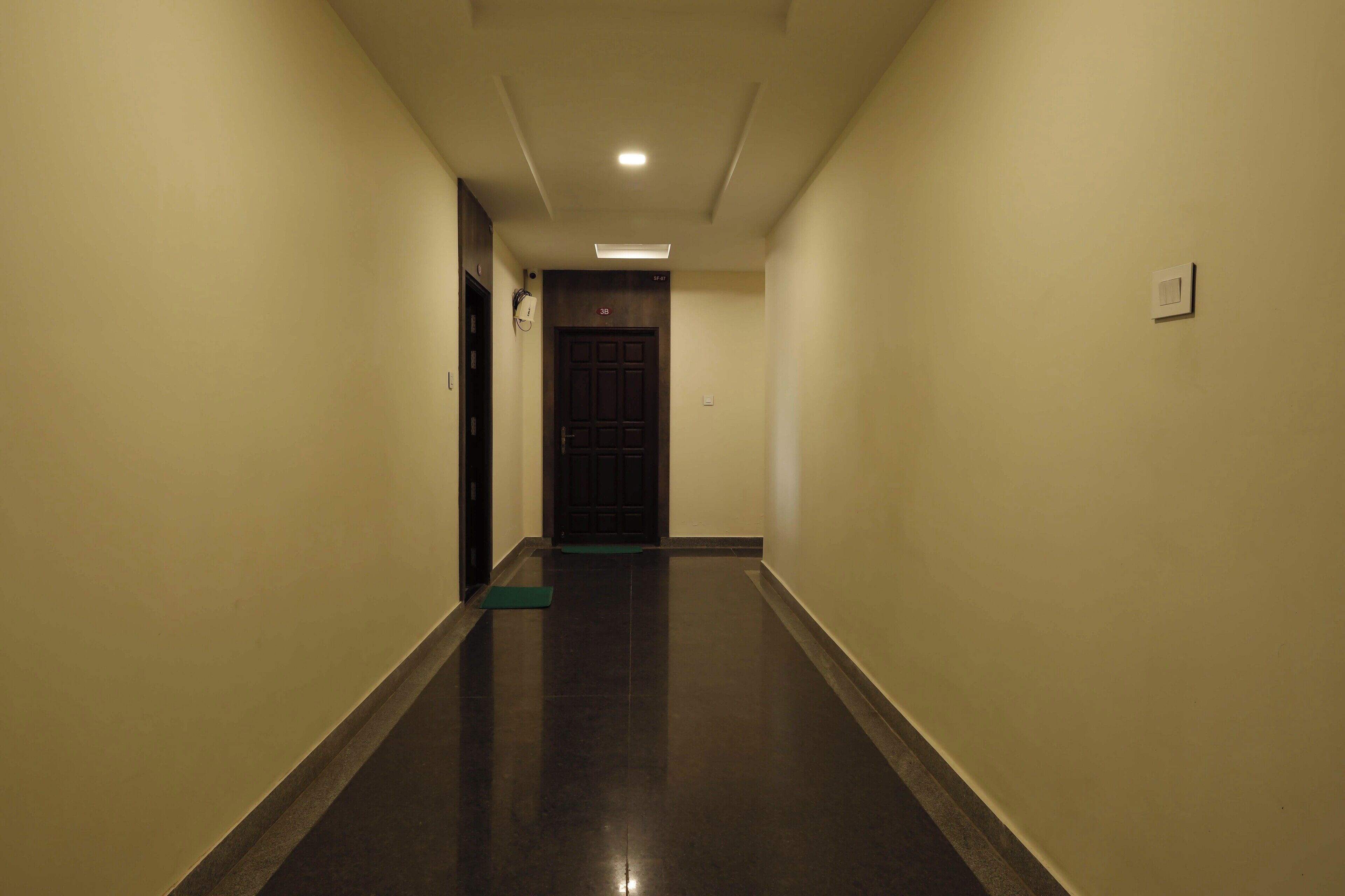 Um corredor com piso escuro, paredes claras e uma porta no final.