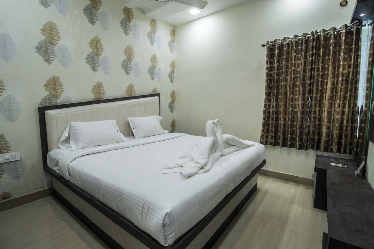 A neatly made bed with white linens and towels, a headboard, and a wall with leaf-patterned wallpaper.
