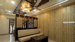 A modern living room with a sofa, a coffee table, a ceiling fan, and patterned wallpaper. - SR Boutique Stay  (Coimbatore)
