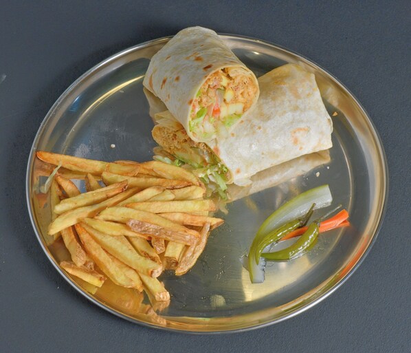Un plato con un wrap, papas fritas y verduras encurtidas.