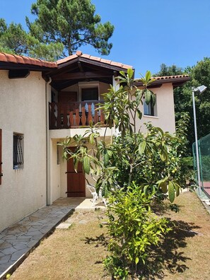 Ein zweistöckiges Haus mit Balkon, einem kleinen Garten und einem Kiesweg, der zum Eingang führt.