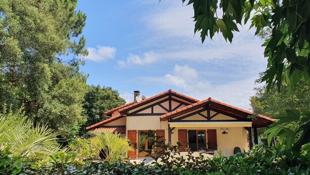 Una casa a due piani con tetto marrone e pareti color beige, immersa nel verde.