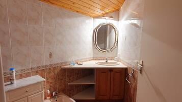 A bathroom with a wooden ceiling, a round mirror, a sink, a bidet, and tiled walls.