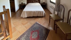 Una camera da letto con soffitto in legno, un letto con copripiumino bianco, due comodini, una finestra con tende e un tappeto decorato sul pavimento.