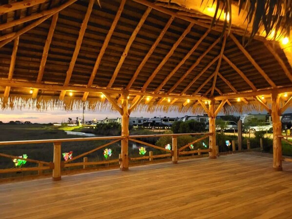 An open wooden deck with a thatched roof, wooden railings, and string lights.