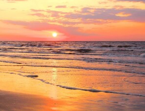 A sunset over the ocean with waves on the shore.