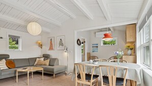 En moderne stue med en grå sofa, et træbord som sofabord og et spiseområde med et hvidt bord og træstole.